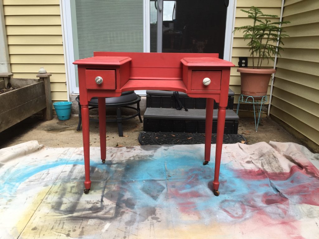 Painted red wooden vanity with two small side drawers and a middle portion, sitting outside on a dropcloth.